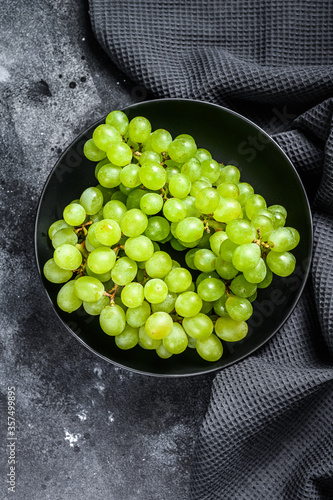 A branch of green juicy grapes in a plate. Black background. Top view