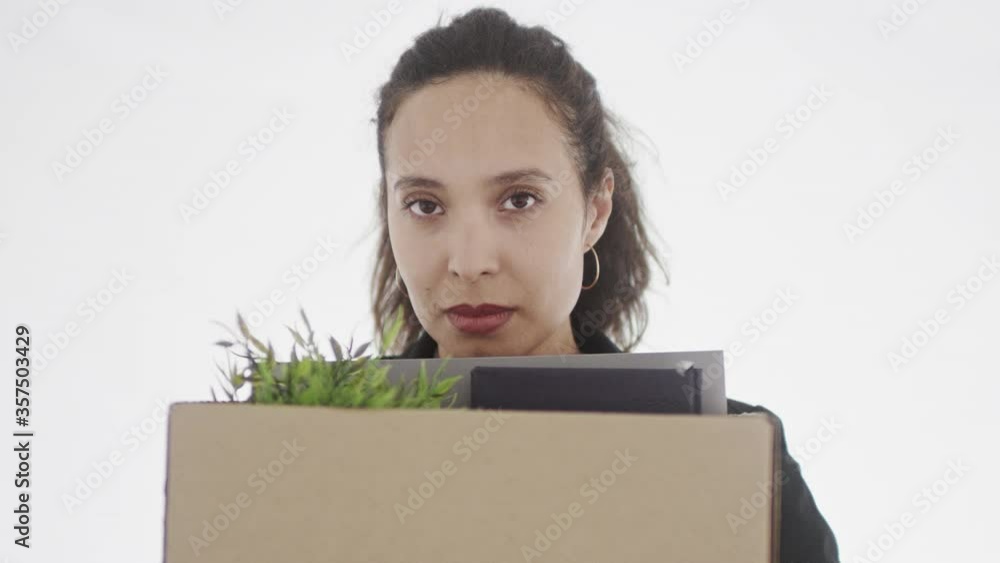 4K portrait of beautiful brunette with brown eyes holding cardboard box with office stuff and looking sorrowfully straight at camera. 4K portrait of beautiful brunette with brown eyes holding cardboard box with office stuff and looking sorrowfully straight at camera.