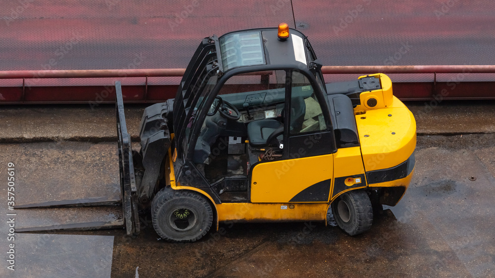 Yellow forklift parked on wet concrete surface. Industrial site.