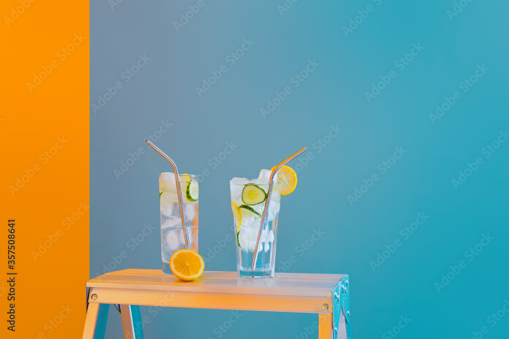 Refreshing tonic and gin Tom Collins cocktail or lemonade with lemon ice and cucumber on contrast colorful blue and yellow background. Bar menu, alcohol recipe decor, specialized website blog design