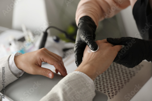 Professional manicurist applying cream on client s hand in beauty salon  closeup