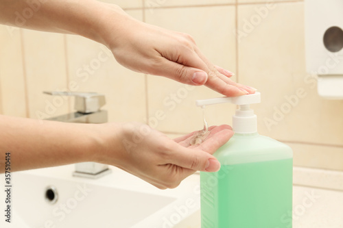 Woman applying antiseptic gel on hand in public bathroom  closeup
