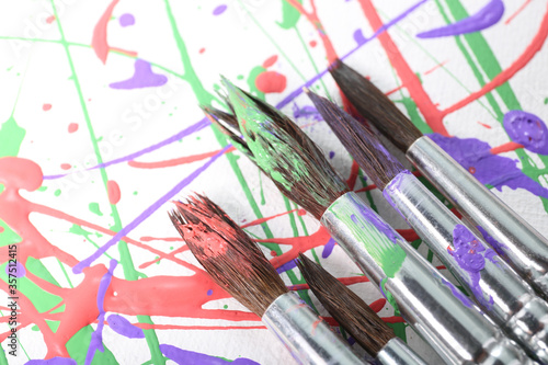 Brushes on canvas with colorful paint splashes, closeup. Art and creativity