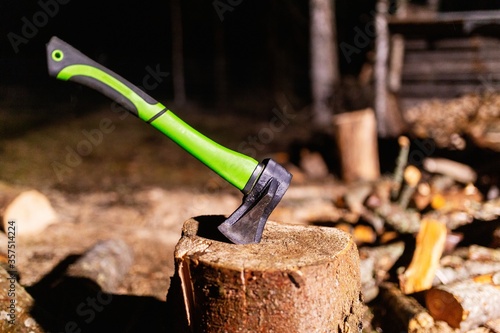 Axe with a strong plastic handle is stuck in a wooden stump against a background of chopped wood. Carpenter's axe for chopping wood is stuck. Sharp axe was stuck in a round old wooden stump