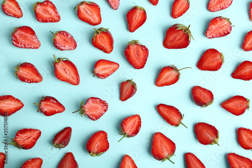 Halves of delicious ripe strawberries on light blue background, flat lay