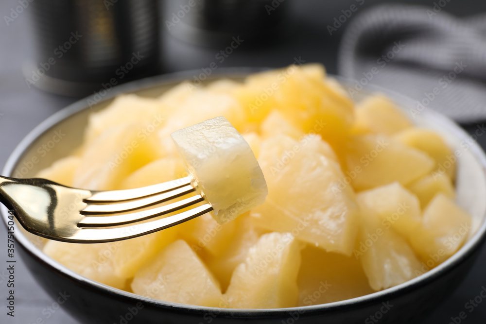 Fork with canned pineapple piece over bowl, closeup Fork with canned pineapple piece over bowl, closeup