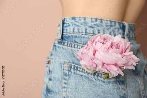Fototapeta Naklejka Na Ścianę i Meble -  Woman with pink peony bud in pocket on beige background, closeup