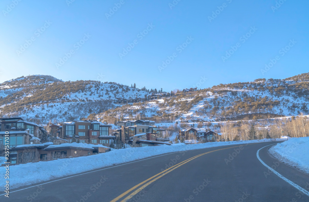Road in Park City passing along snowed in mountain slopes with homes and trees