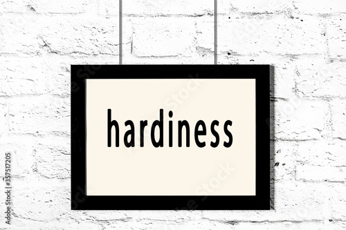 Black frame hanging on white brick wall with inscription hardiness