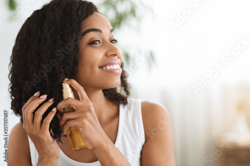 Hair Care. Happy Afro Woman Using Oil For Split Ends At Home photo