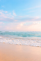 Sandy beach, blue cloudy sky and soft ocean wave with warm sunset light.