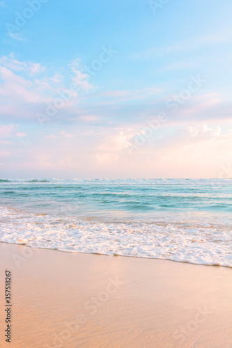 Sandy beach, blue cloudy sky and soft ocean wave with warm sunset light.
