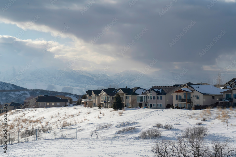 Homes on snowy terrain ovelooking Wasatch Mountain peak and dark overcast sky