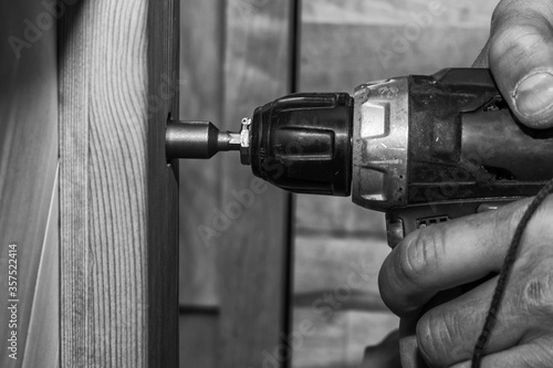 old cordless screwdriver in a worker?s hand, twists a screw into wooden, black and white photo
