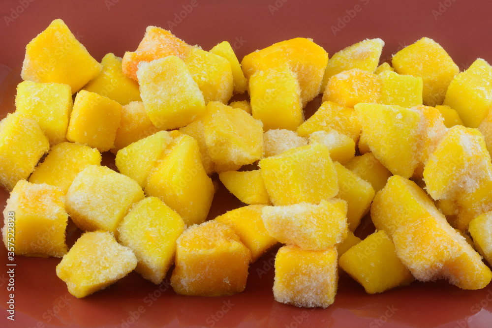 Closeup of frozen mango fruit chunk cubes with ice crystals on red plate Closeup of frozen mango fruit chunk cubes with ice crystals on red plate