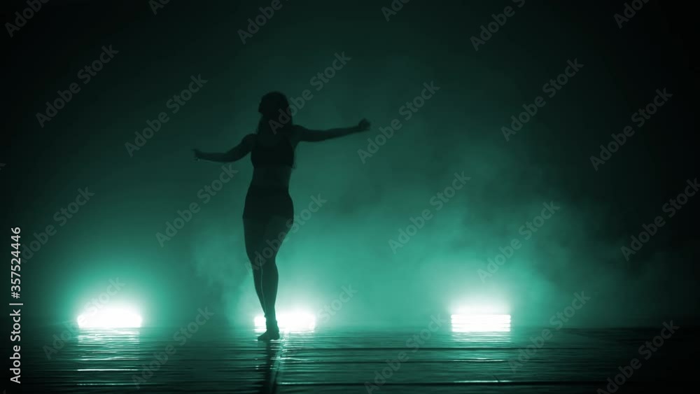 Beautiful fit female silhouette is dancing modern contemporary choreography in dusk of dance studio Beautiful fit female silhouette is dancing modern contemporary choreography in dusk of dance studio