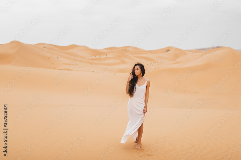 Beautiful woman in gentle silk dress walking in sand dunes of Morocco Sahara desert. Brunette with long hair, eastern appearance. Beautiful woman in gentle silk dress walking in sand dunes of Morocco Sahara desert. Brunette with long hair, eastern appearance.