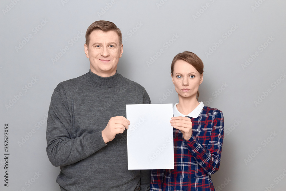 Portrait of adult couple holding together white blank paper sheet Portrait of adult couple holding together white blank paper sheet
