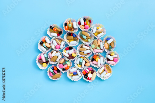 Colorful tablets with capsules and pills in cupcake wrappers on blue background.