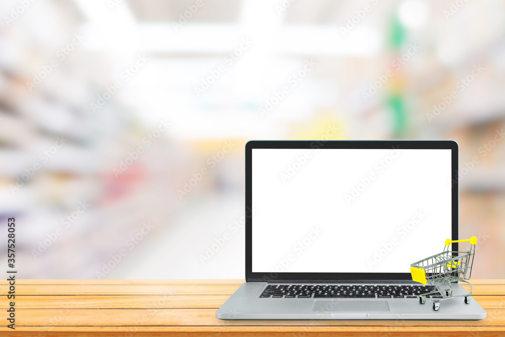 Shopping Online Concept : Yellow shopping cart put on laptop with blank white screen and blurry image in background. Shopping Online Concept : Yellow shopping cart put on laptop with blank white screen and blurry image in background.