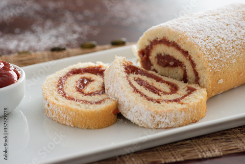 delicious roll cake with guava cream jelly and sugar sliced on white platter and blurred background