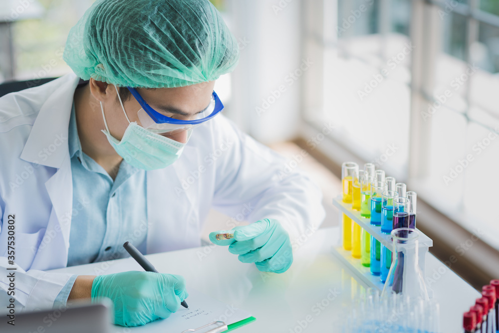 Professional Asian scientist or researcher man in work coat uniform examine liquid sample and record result detail in science lab Professional Asian scientist or researcher man in work coat uniform examine liquid sample and record result detail in science lab