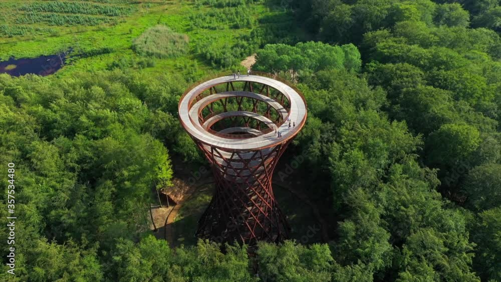 Aerial tilt up shot of people at spiral observation tower amidst green trees, drone flying backward from famous landmark in forest on sunny day - Copenhagen, Denmark