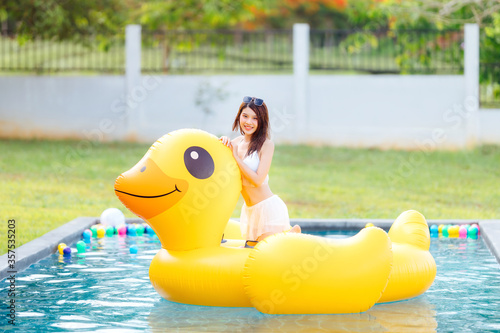 Beautiful Asian woman wear white swimsuit with sunglasses sit on yellow duck in the pool