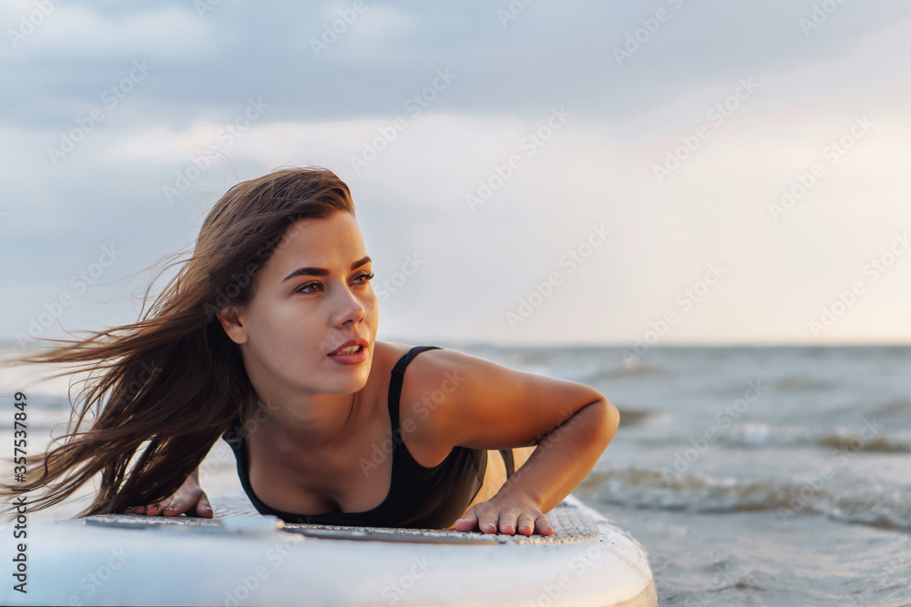 Young sexy woman surfer lying on her sup board looking to the sunset. Rest at nature concept