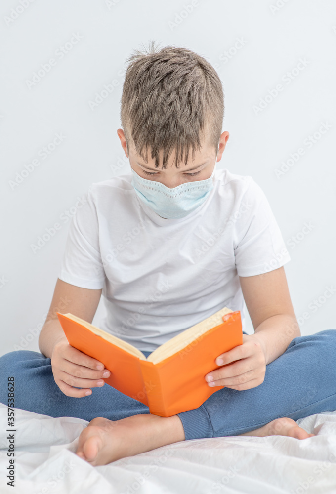 Sick boy wearing medical protective mask sits on a bed at home and reads a book. Quarantine and coronavirus epidemic concept Sick boy wearing medical protective mask sits on a bed at home and reads a book. Quarantine and coronavirus epidemic concept