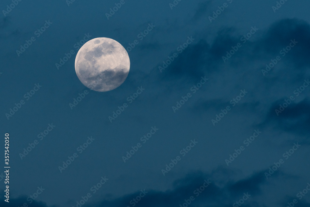 A full moon in a cloudy blue sky background