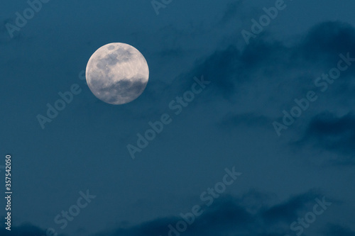 A full moon in a cloudy blue sky background