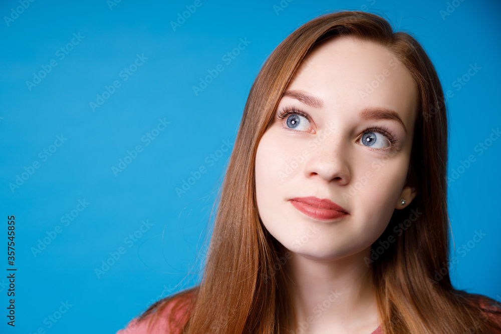 Young ginger girl in pink t-shirt studio portait isolated on blue wall background, looking away. Young ginger girl in pink t-shirt studio portait isolated on blue wall background, looking away.