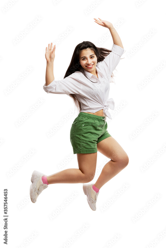 Laughing young girl in a white shirt and green shorts is jumping. Brunette with long hair. Isolated on a white background. Vertical.