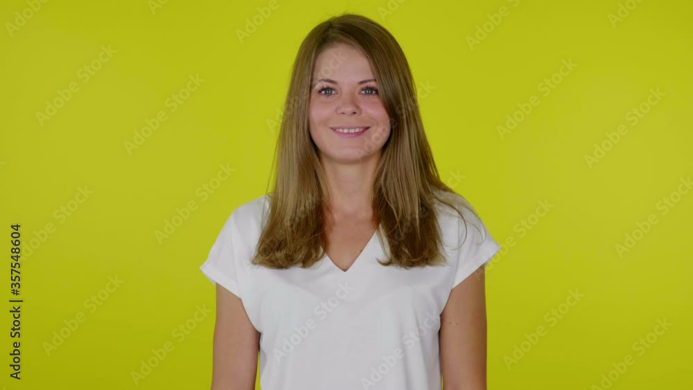 Brunette woman in a white T-shirt is looking at the camera and smiling on a yellow background with copy space. Place for text or product. 4K slow motion footage Brunette woman in a white T-shirt is looking at the camera and smiling on a yellow background with copy space. Place for text or product. 4K slow motion footage