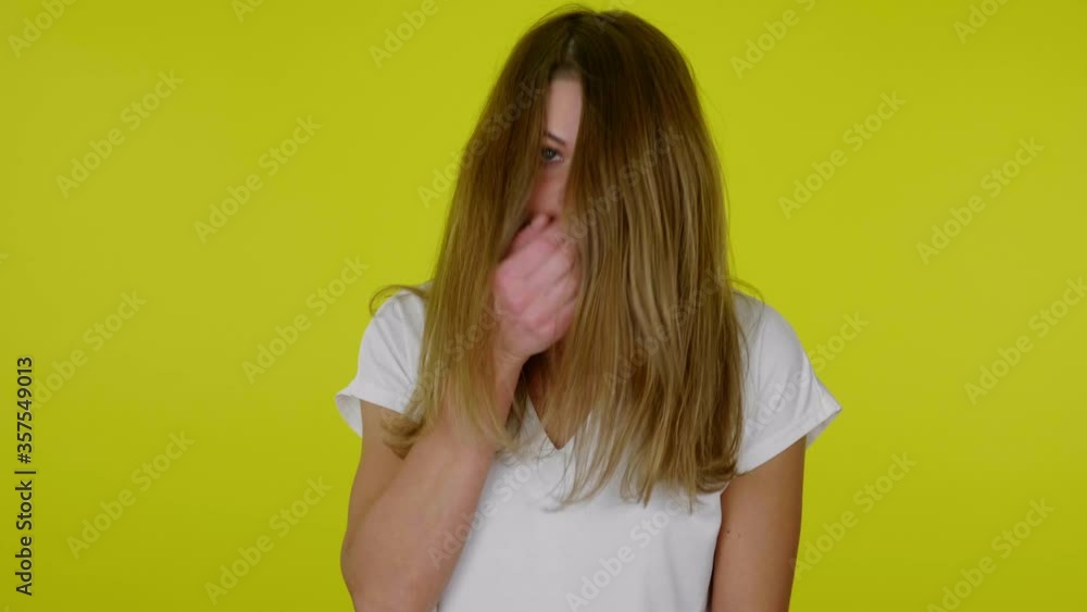 Sick brunette woman in a white T-shirt sneezes closing mouth with a palm on a yellow background with copy space. Place for text or product. 4K slow motion footage Sick brunette woman in a white T-shirt sneezes closing mouth with a palm on a yellow background with copy space. Place for text or product. 4K slow motion footage