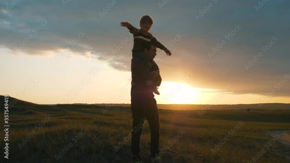 Silhouette of a happy family at sunset. The son sits on the shoulders of his father and depicts the flight of an airplane. The family is relaxing in the fresh air, dreaming of traveling. Silhouette of a happy family at sunset. The son sits on the shoulders of his father and depicts the flight of an airplane. The family is relaxing in the fresh air, dreaming of traveling.