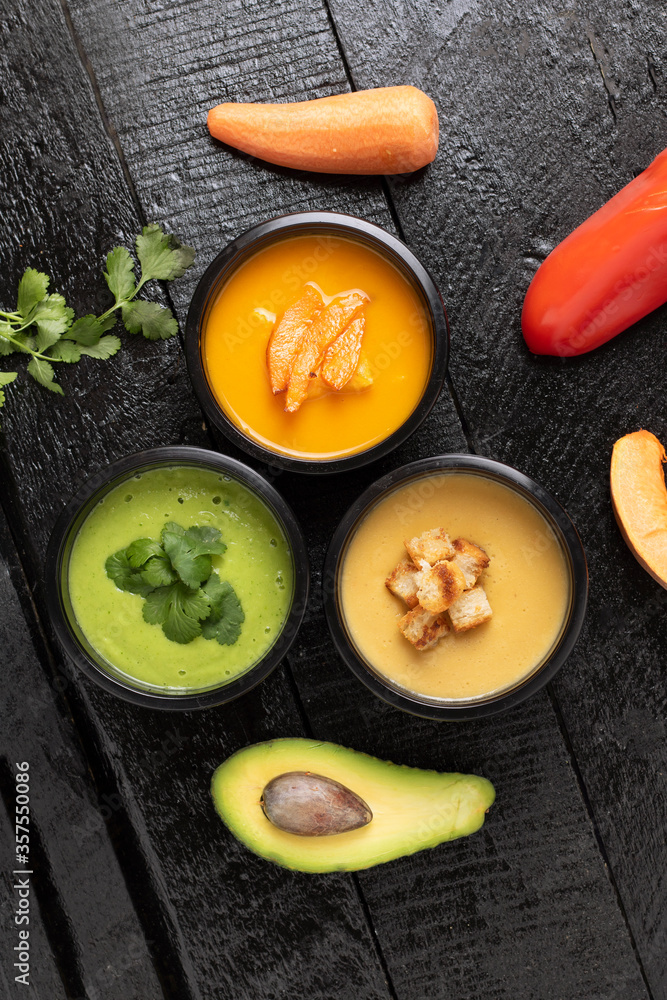 Spinach cream soup, pumpkin and avacado soups in food containers, flat lay. Wooden background, vertical Spinach cream soup, pumpkin and avacado soups in food containers, flat lay. Wooden background, vertical