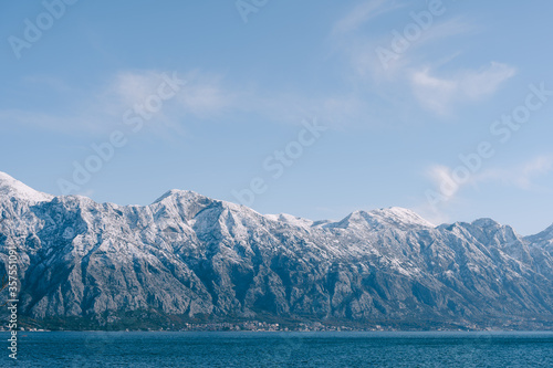 Snow-capped mountain peaks in Kotor Bay, Montenegro, above the city of Dobrota. An assiable and fish farm in the sea.