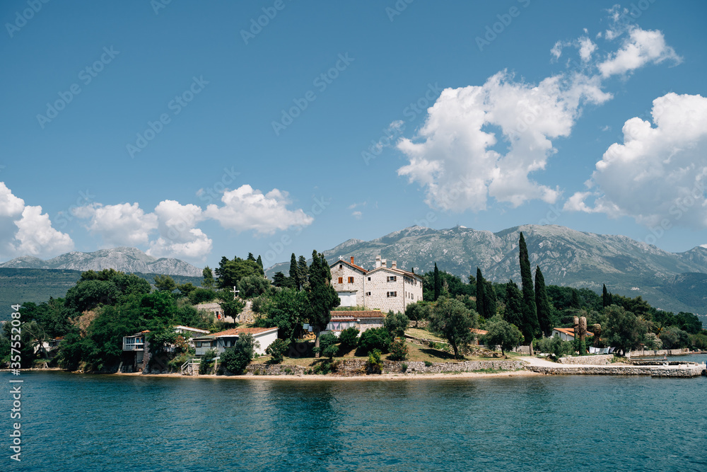 A villa on top of a mountain, on an island in the sea. The shore of the island, the view from the water, the blue sky and the white clouds above the mountains.