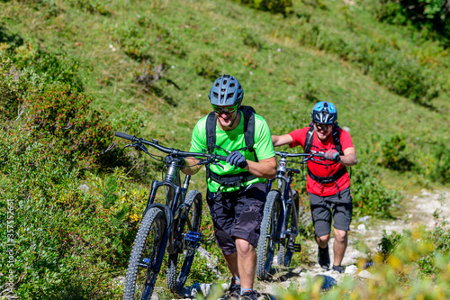 Zwei gutgelaunte Mountainbiker schieben ihre Bikes bergauf