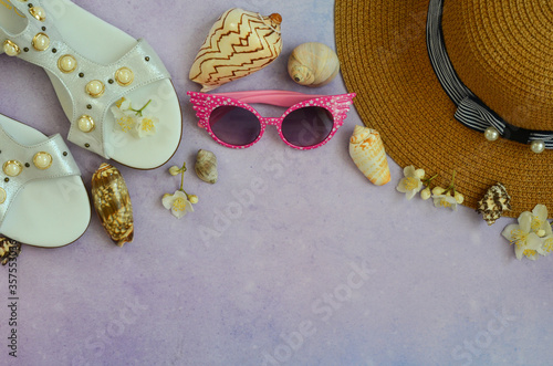Summer background with space for text straw women's hat, white flowers, shells and women's sandals and glasses top view. Accessories for leisure and tourism
