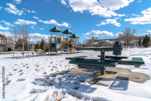 Playground and picnic table with footprints on the snow covered ground in winter