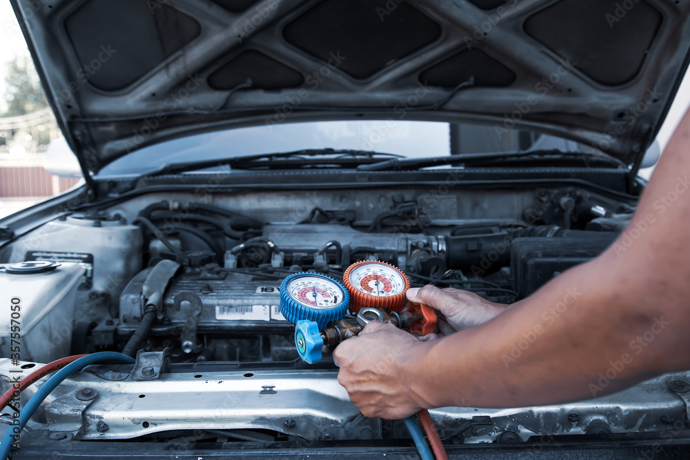Auto mechanic using measuring equipment tool for filling car air conditioners fix checking. Concepts of car care repair service and insurance.