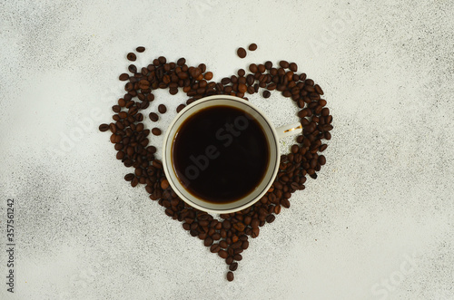 Heart shaped coffee beans and cup of coffee on a light grey background. Space for text top view