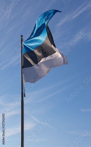 Estonian blue black white flag waving in the wind on a blue summer sky background