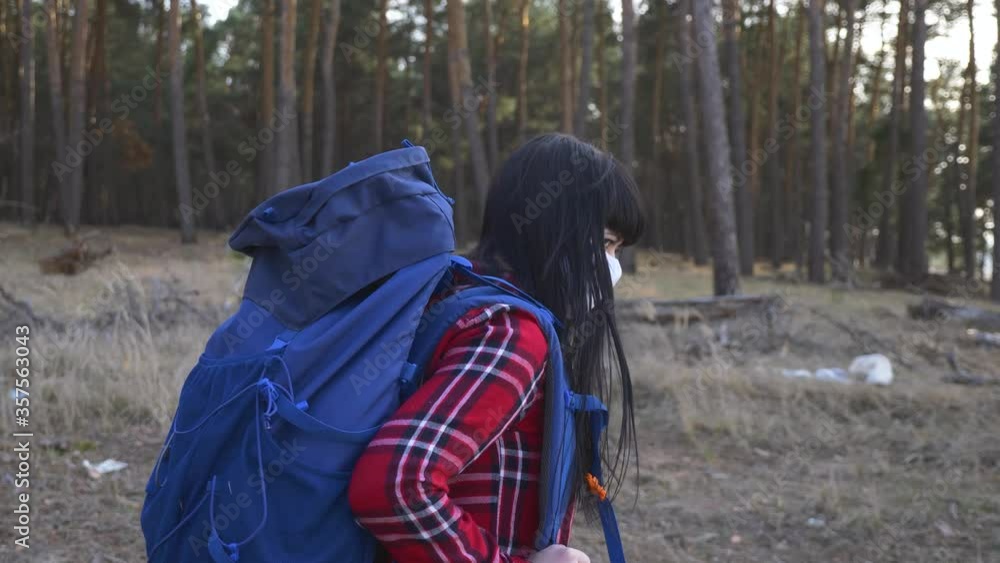 A young woman with a backpack and wearing a mask on her face through a pine forest, enjoying the landscape to protect herself from infection. A young woman with a backpack and wearing a mask on her face through a pine forest, enjoying the landscape to protect herself from infection.