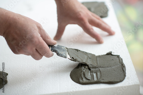 A man putsglue with putty knife on foam to stick it to the ceiling. Styrofoam, seiling mounting. A man glues foam. Ceiling insulation. Warming. Repair in the house. Male hands with tools. DIY repair