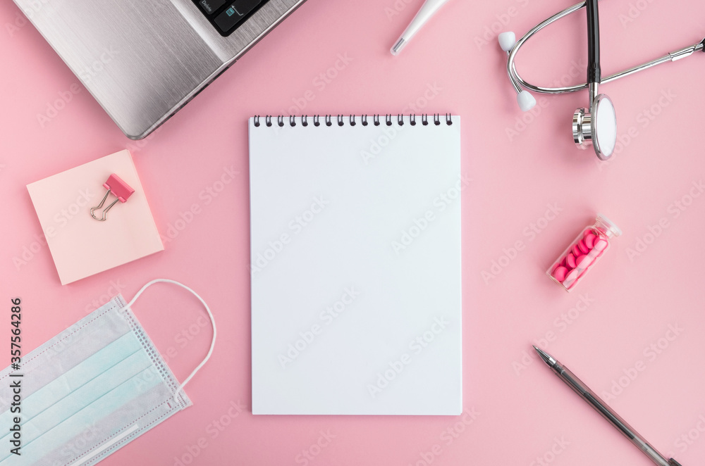 Doctor workplace and medical equipment on pink background. Blank notepad, stethoscope, laptop, protective face mask, thermometer, pills and pen on table. Top view, flat lay, copy space Doctor workplace and medical equipment on pink background. Blank notepad, stethoscope, laptop, protective face mask, thermometer, pills and pen on table. Top view, flat lay, copy space