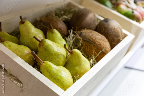 Green pears and coconuts are in a wooden box.